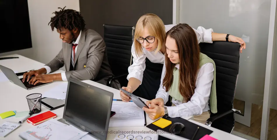 Three office professionals reviewing documents and tablets at a desk, representing employees' compensation claim bills and workplace legal processes