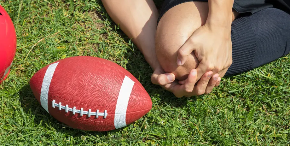 Injured football player clutching knee on grass beside a football, representing Super Bowl injuries and safety tips for players