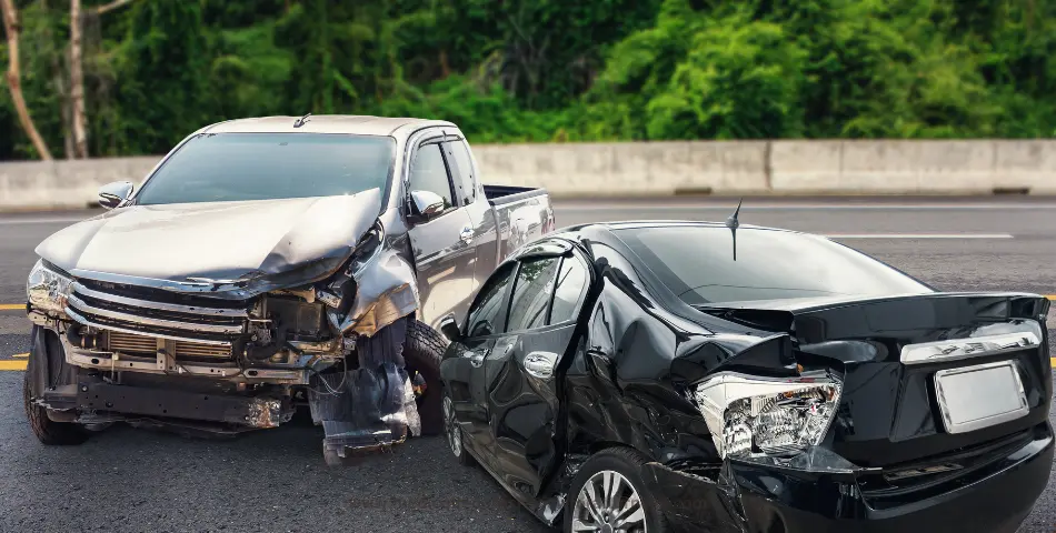 Severely damaged silver truck and black sedan after a collision on a road, representing witnesses in car crash lawsuits and injury claims