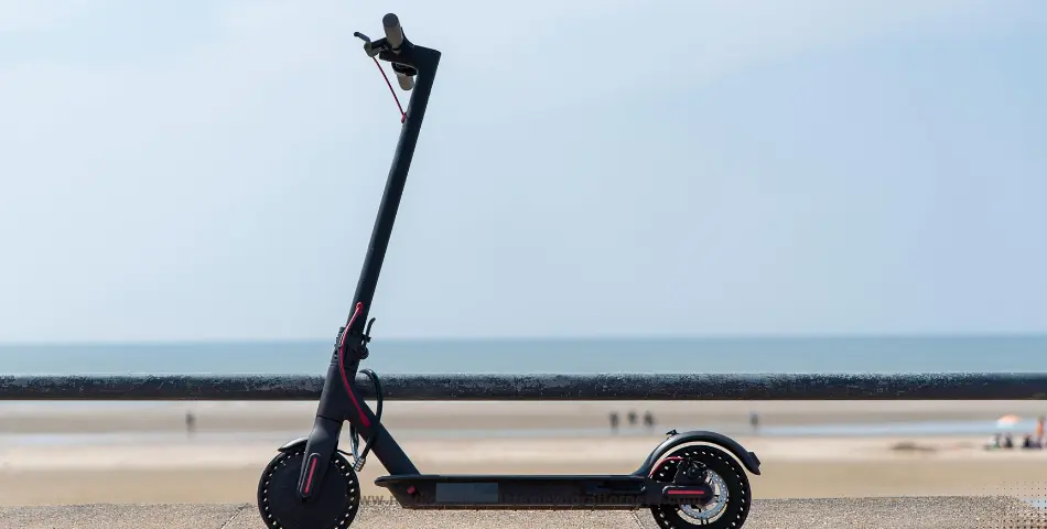 Black electric scooter parked on concrete near beach and calm sea, illustrating electric skateboard lawsuit