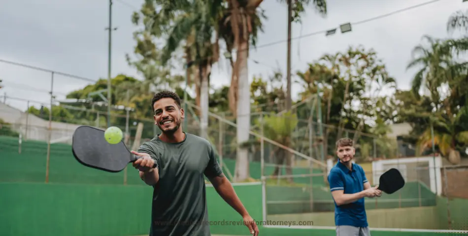 Two men playing pickleball on outdoor court with palm trees and fencing, illustrating pickleball injuries