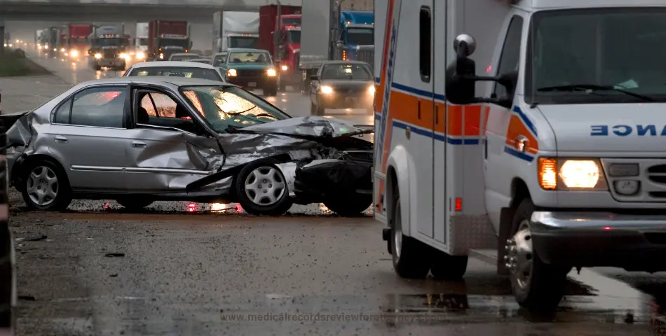 Badly damaged silver car on a rainy highway beside an ambulance, representing vehicle accidents and personal injury claims