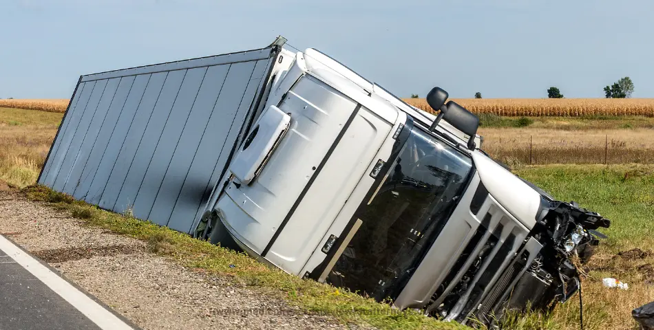 Large cargo truck overturned off road near farmland under clear sky, illustrating injury compensation case