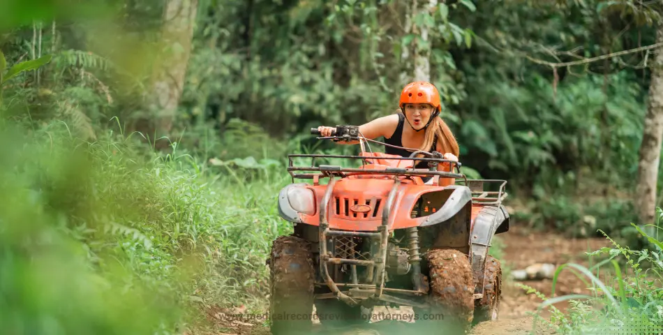 Individual riding muddy all-terrain vehicle on narrow path through dense foliage, illustrating ATV accident cases