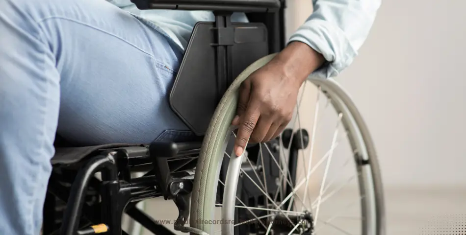 Hand gripping wheelchair wheel with person wearing light blue pants, representing paralysis and mobility challenges