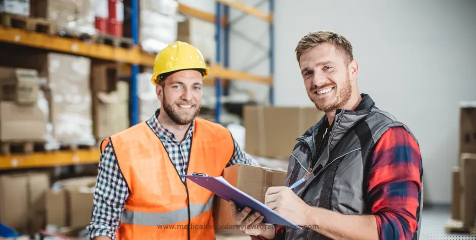 | Two men managing warehouse stock, one writing on clipboard and another in protective gear, illustrating workers’ compensation retaliation
